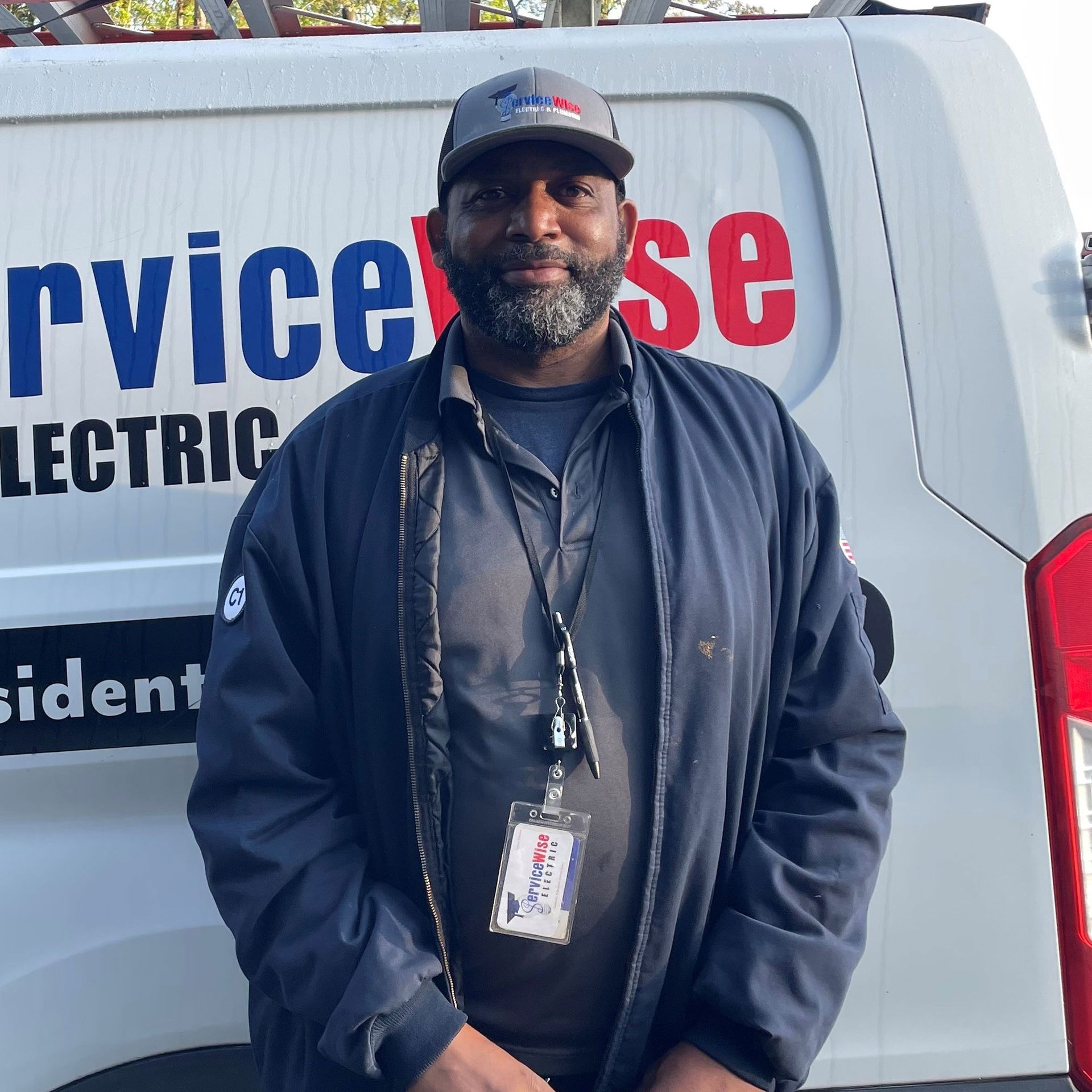 Man in navy jacket and cap stands next to a white van with red