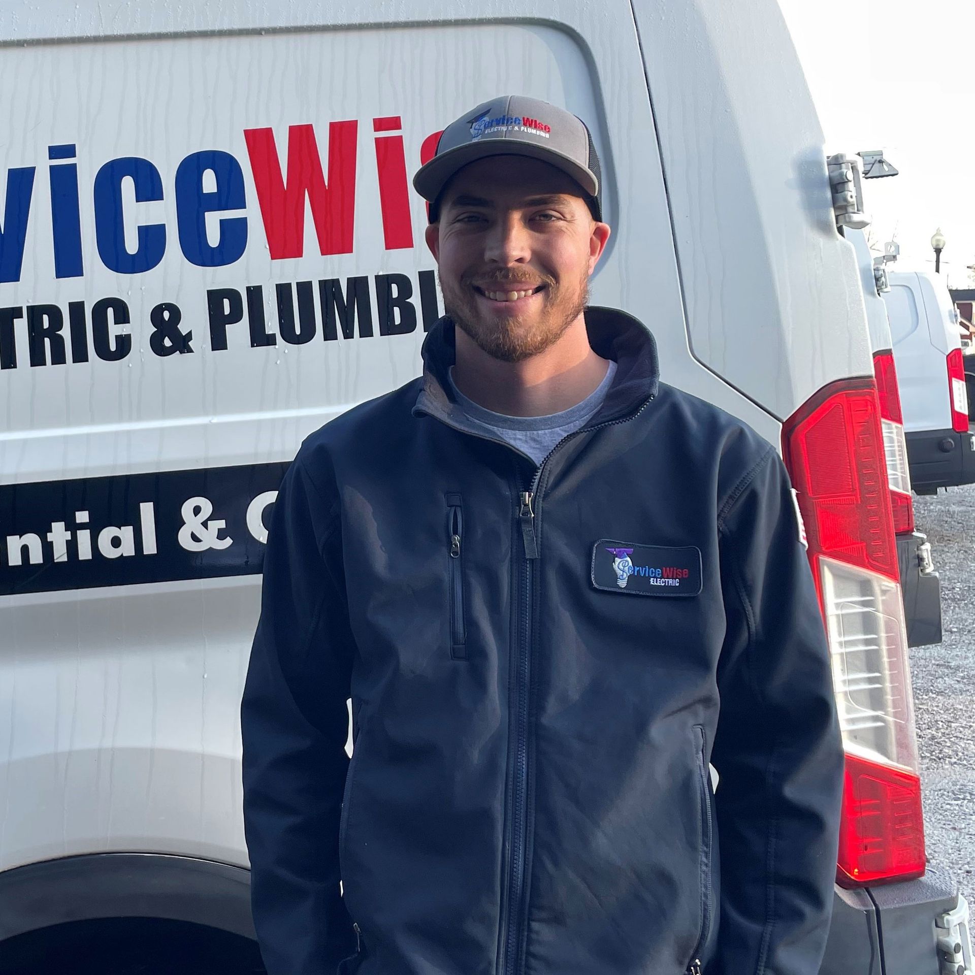 Man in a ServiceWise uniform stands in front of a company van. He is smiling.