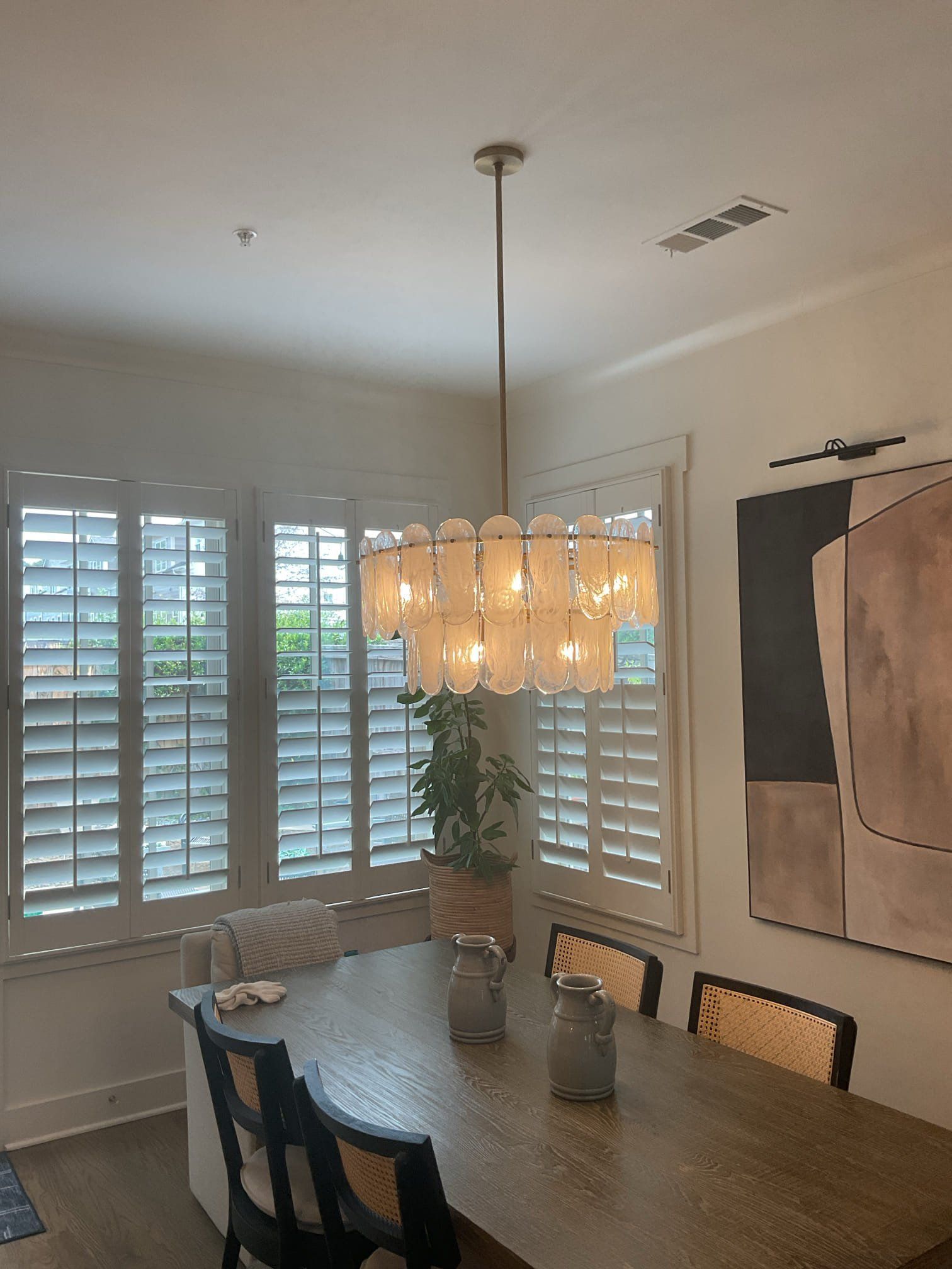 Dining room with chandelier over a wooden table, chairs, and shuttered windows.
