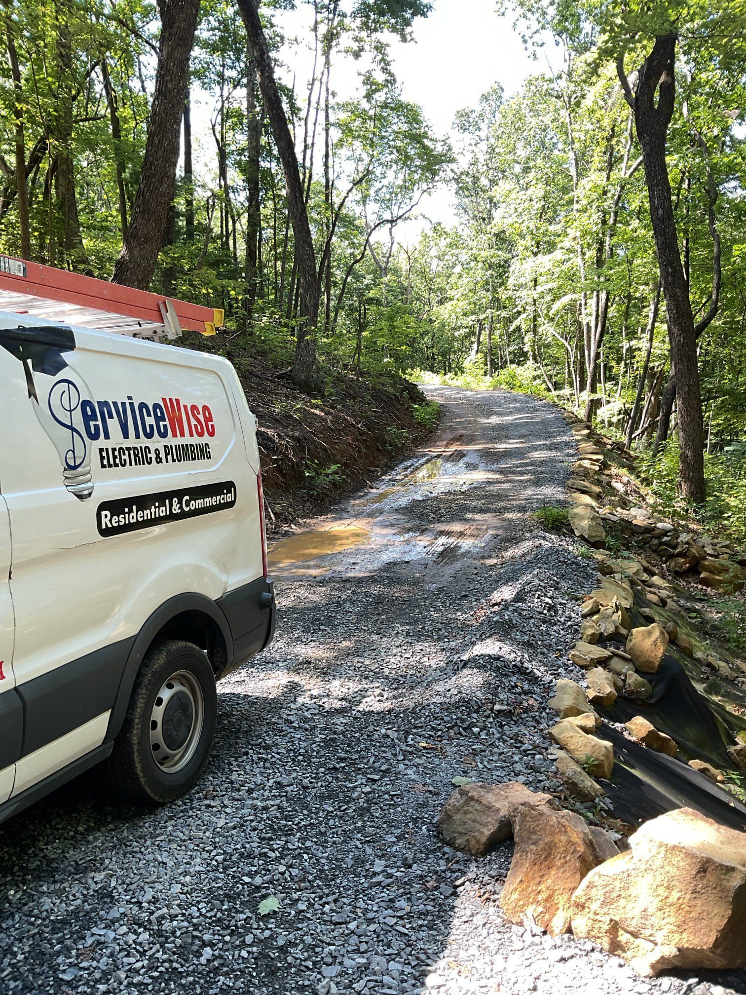 Service Bros. van parked on a gravel driveway in a wooded area. A ladder is on top of the van.