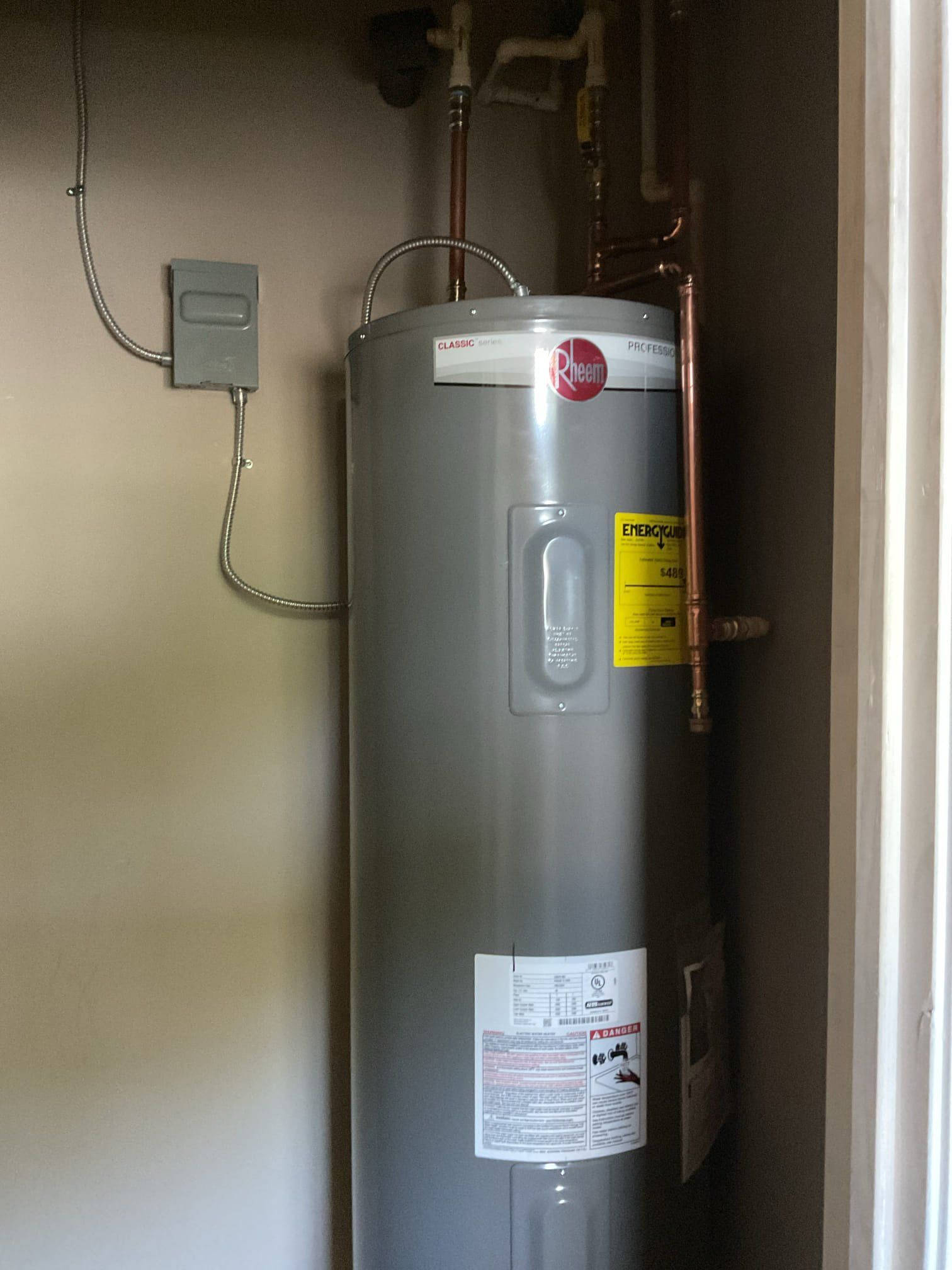 Silver water heater in a corner, with copper pipes and electrical box visible.