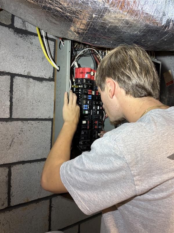 Man working on an electrical panel attached to a cinder block wall.