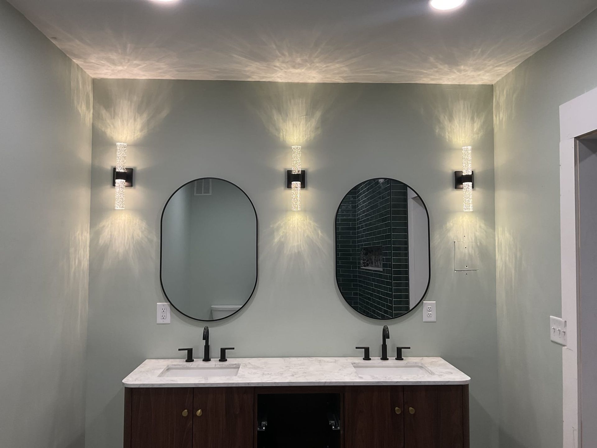Bathroom with two oval mirrors, sconce lighting, and a dark wood vanity.