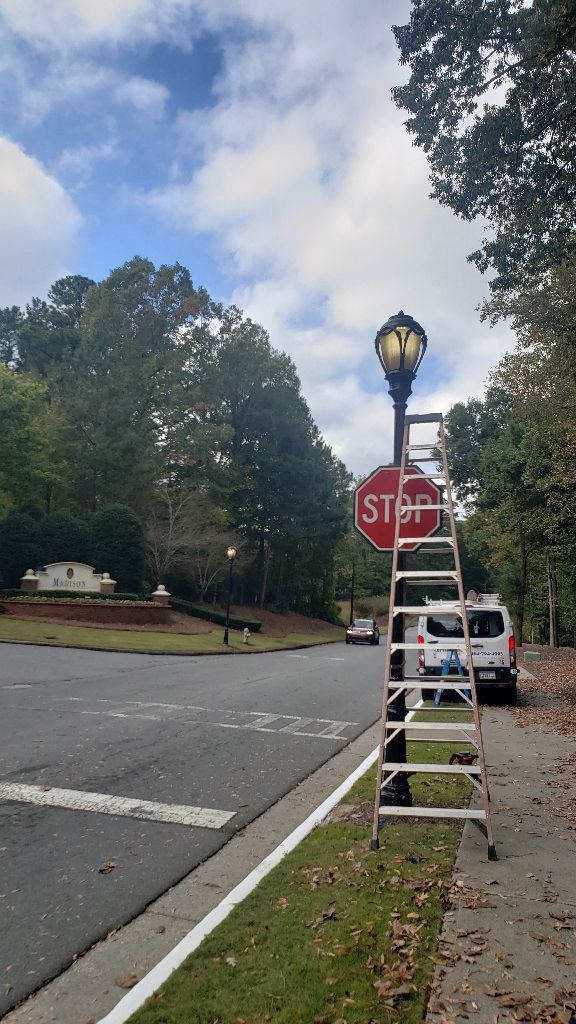 Ladder next to a lamppost and stop sign at an intersection. A white van is parked nearby.