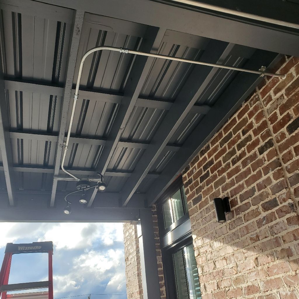 Electrical conduit runs across a dark-colored outdoor ceiling, next to a brick wall.