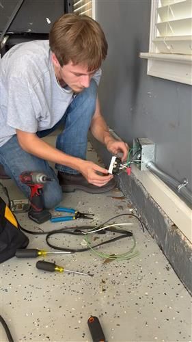 Electrician working on wiring in a garage, using tools.