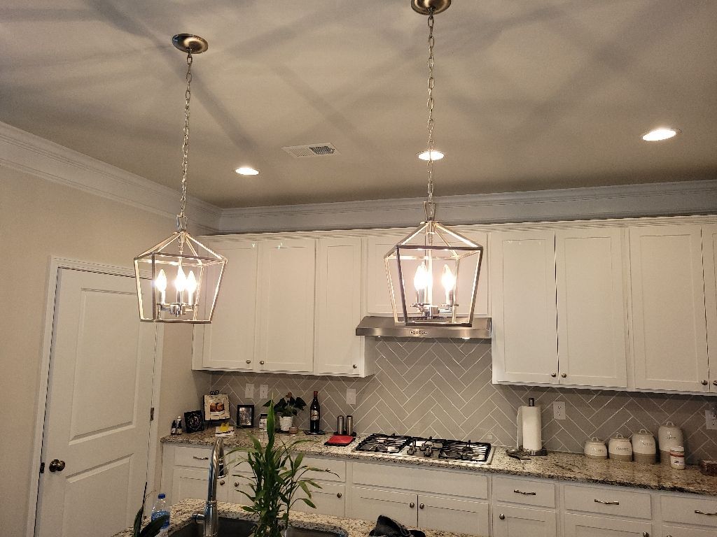 Kitchen with white cabinets, pendant lights, and a herringbone backsplash.