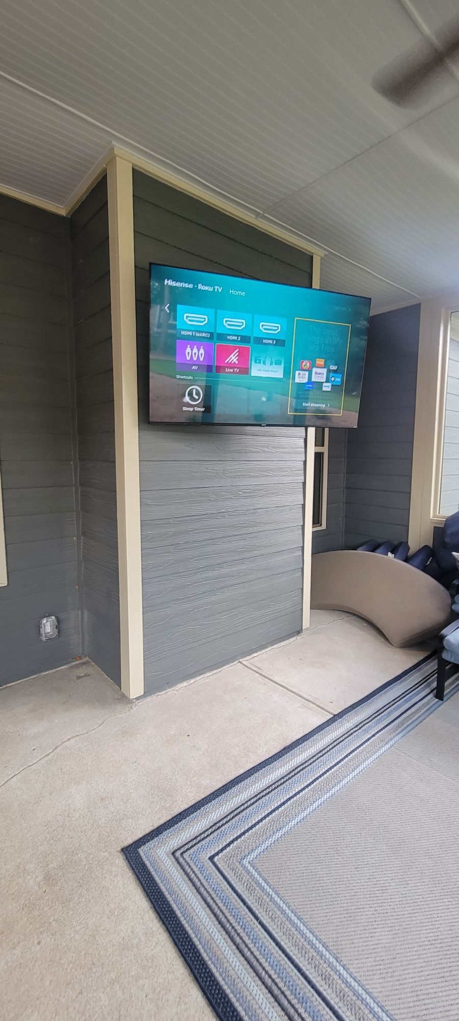 TV mounted on a gray wall in an outdoor living space with a rug and seating.