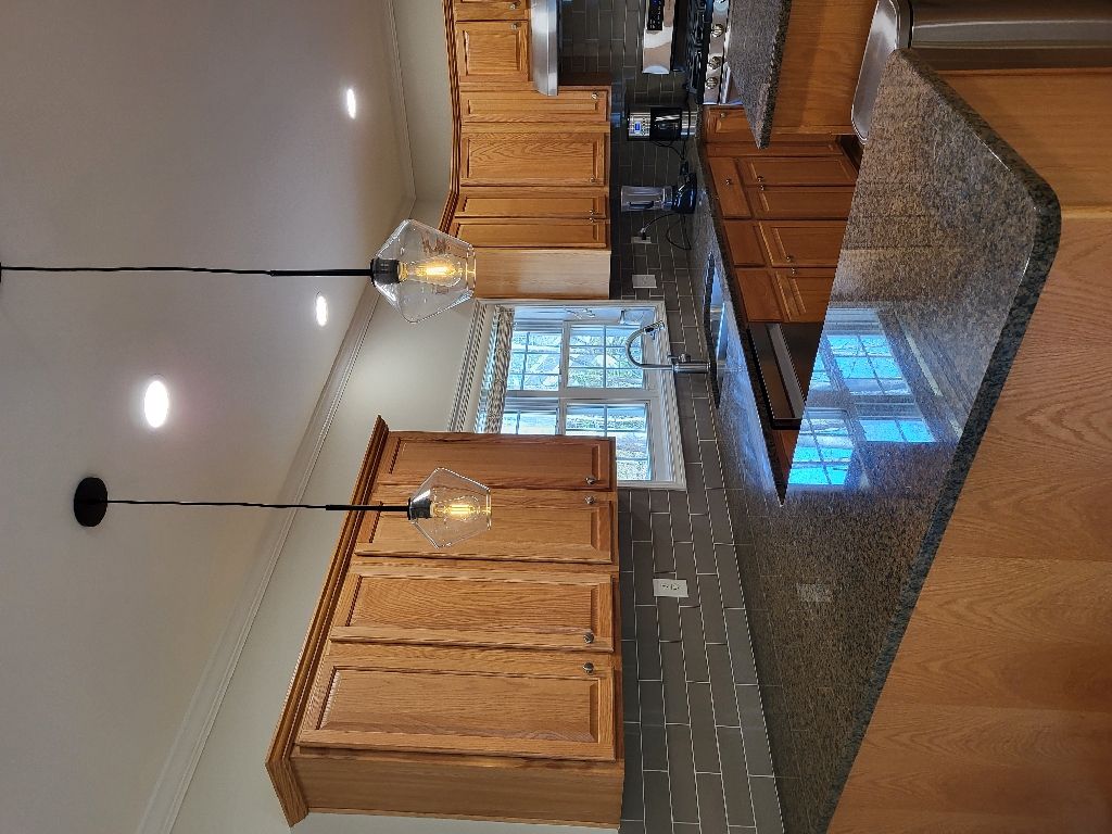Kitchen with wooden cabinets, dark countertops, two hanging lights, and a window.