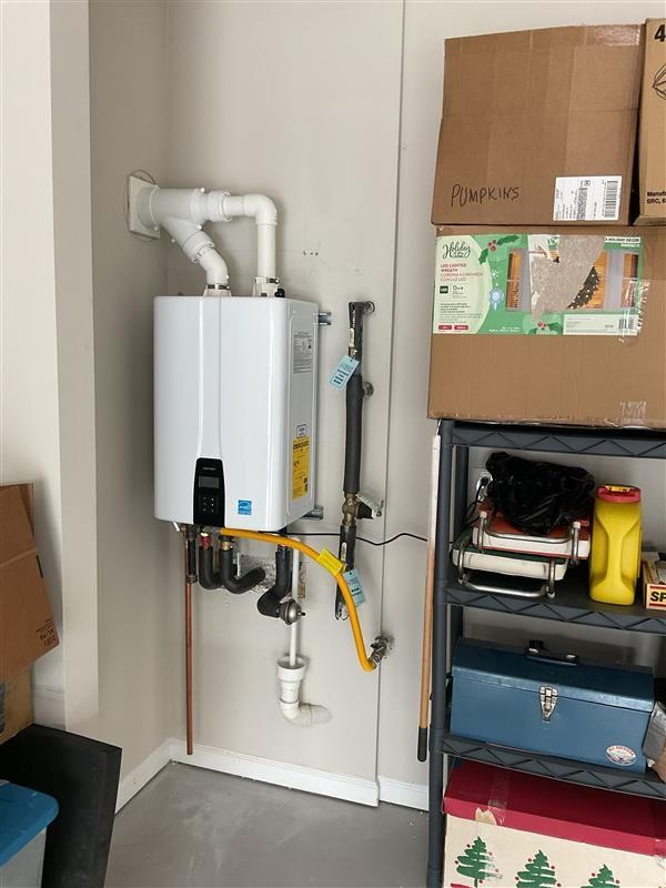 White tankless water heater mounted on a beige wall in a garage, next to shelves and boxes.