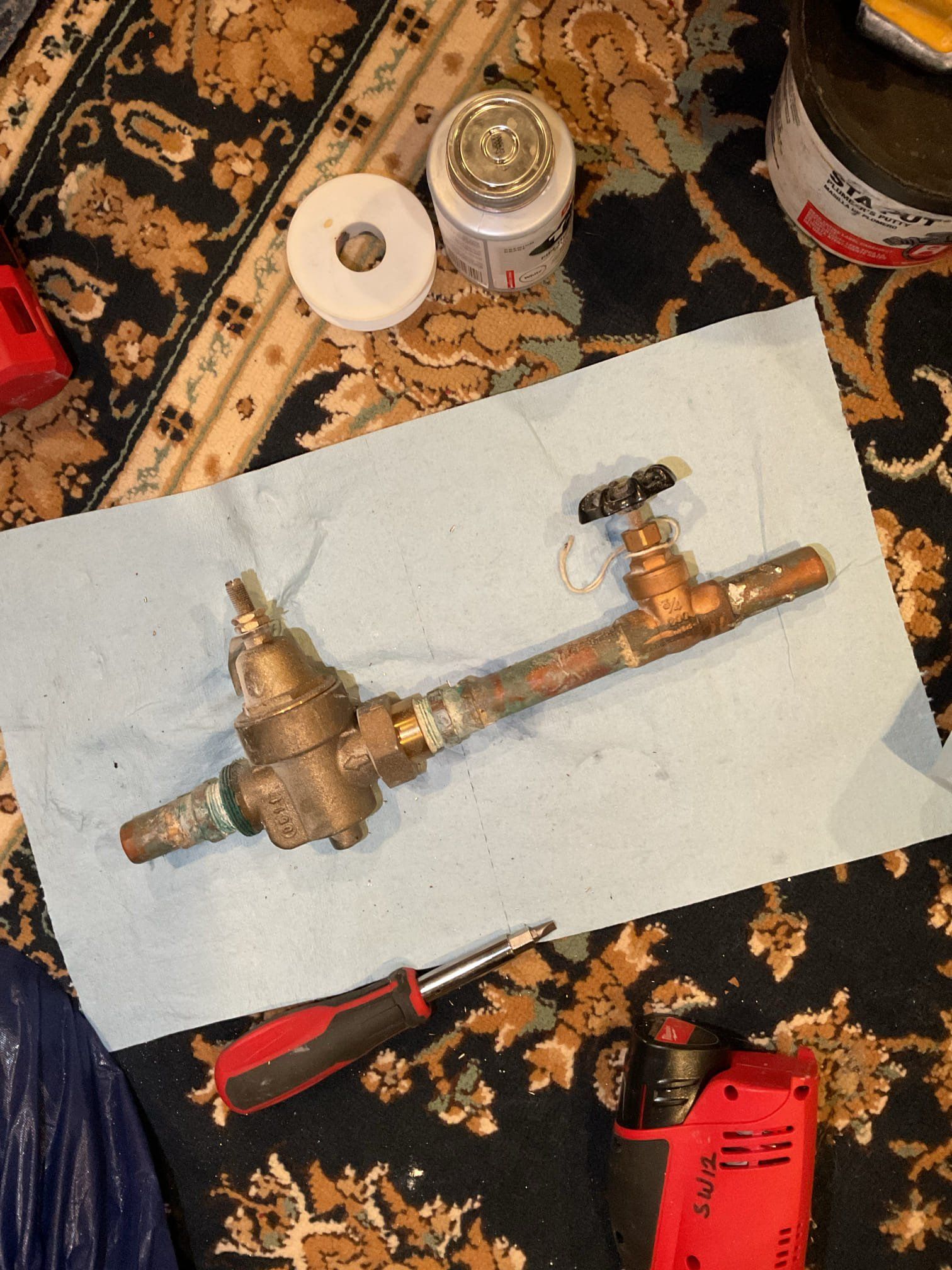 Copper plumbing assembly with a water pressure regulator and valve, lying on a blue shop towel, surrounded by tools.