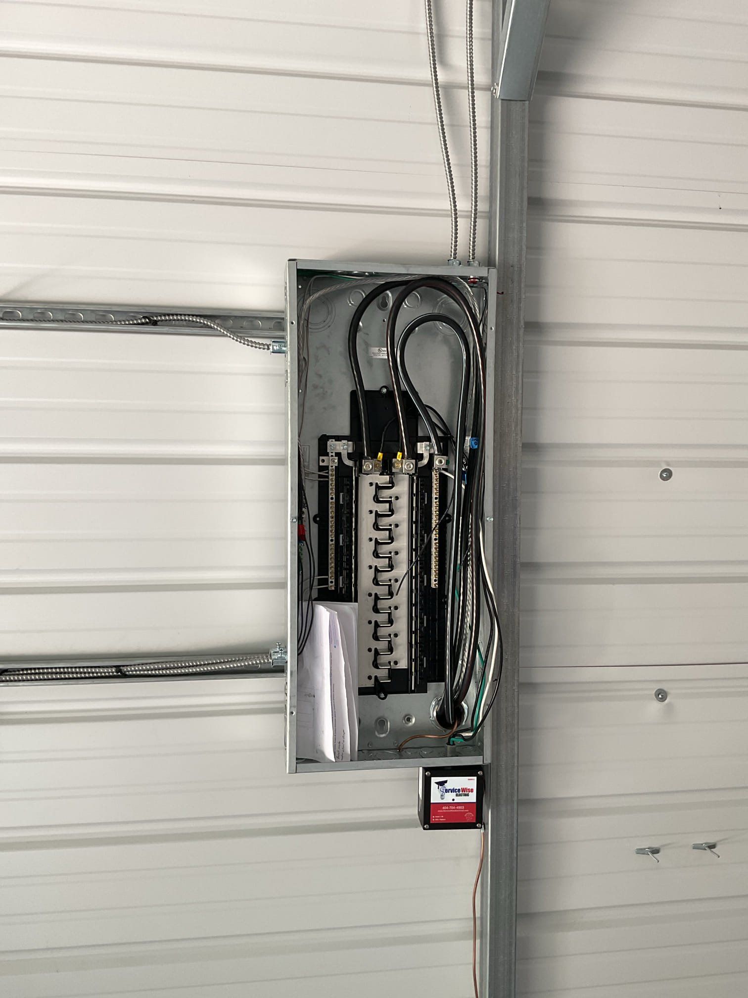Electrical panel mounted on a corrugated metal wall. Wires are connected inside.