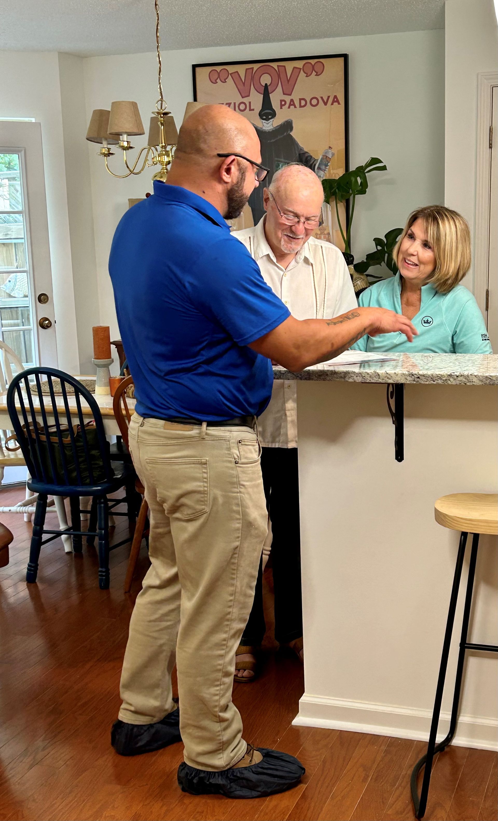Man in blue shirt speaks to an older couple at a kitchen counter.