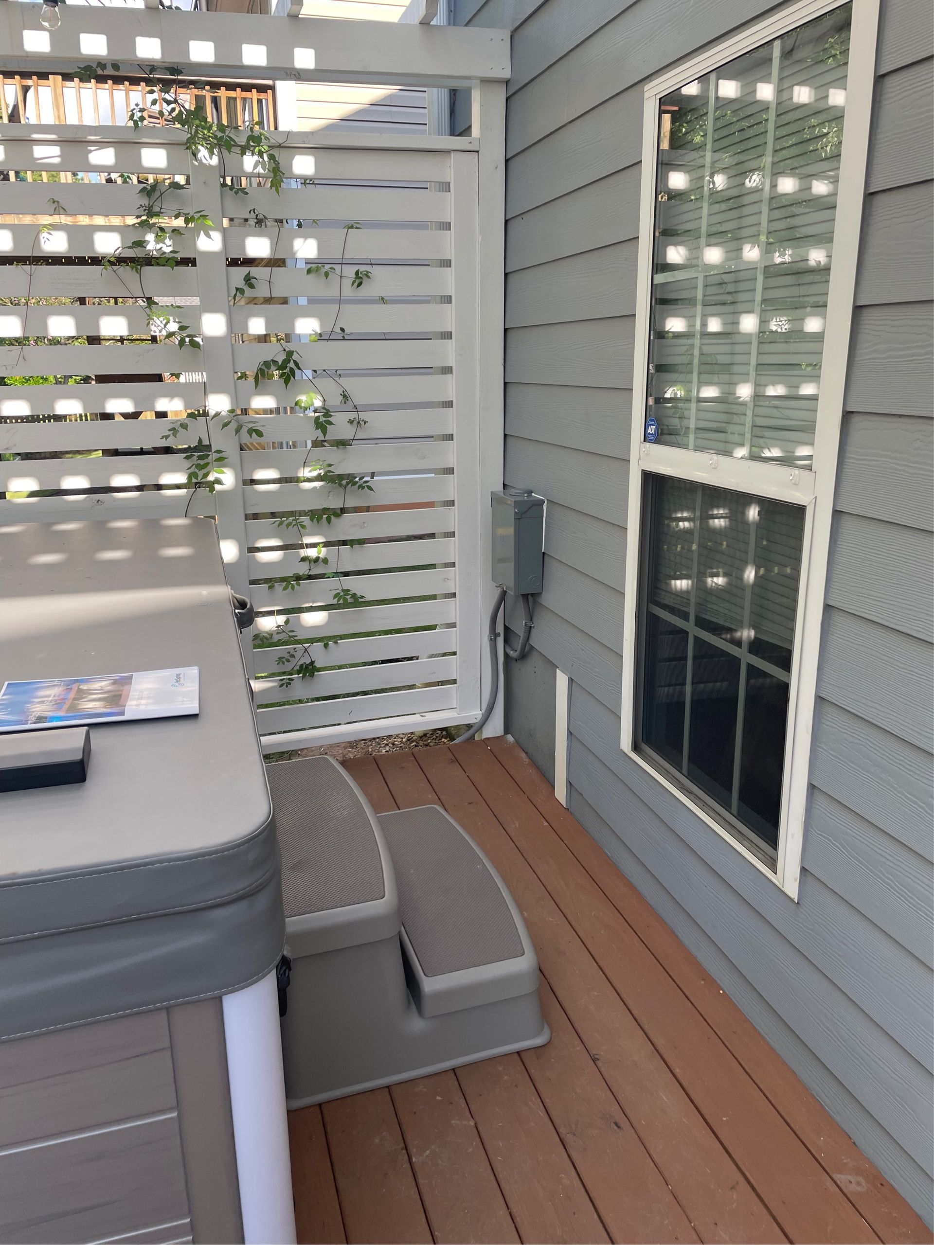 Hot tub with steps on a wood deck next to a window and privacy screen.