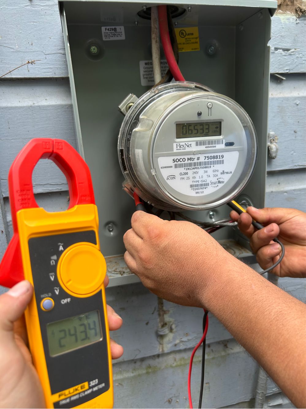 Electric meter being tested with a clamp meter displaying a reading of 243.4 amps.