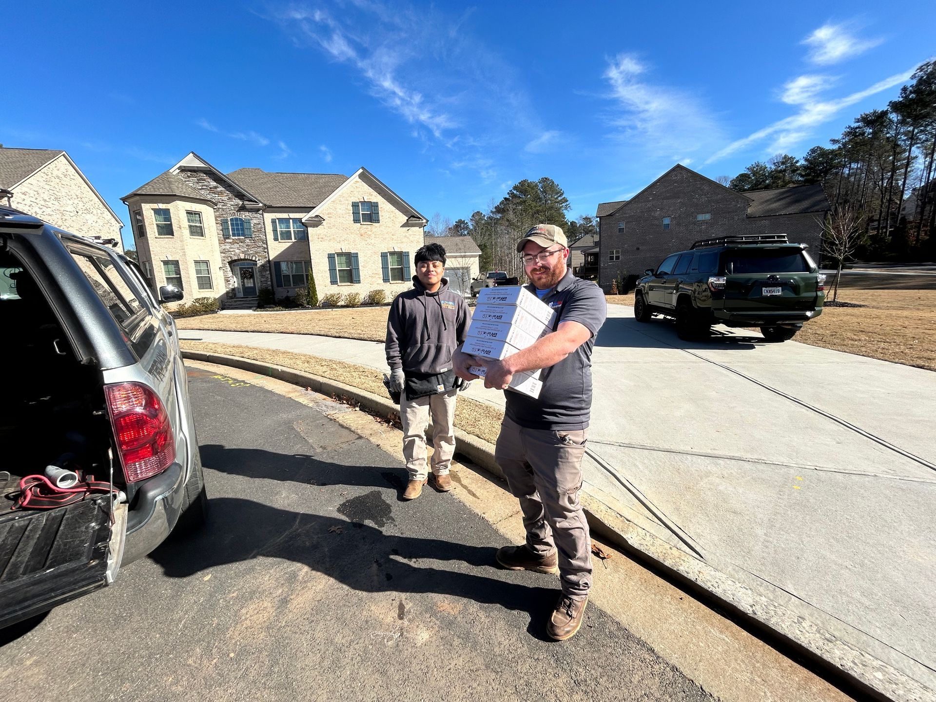 Two men unload boxes from a vehicle on a sunny residential street.