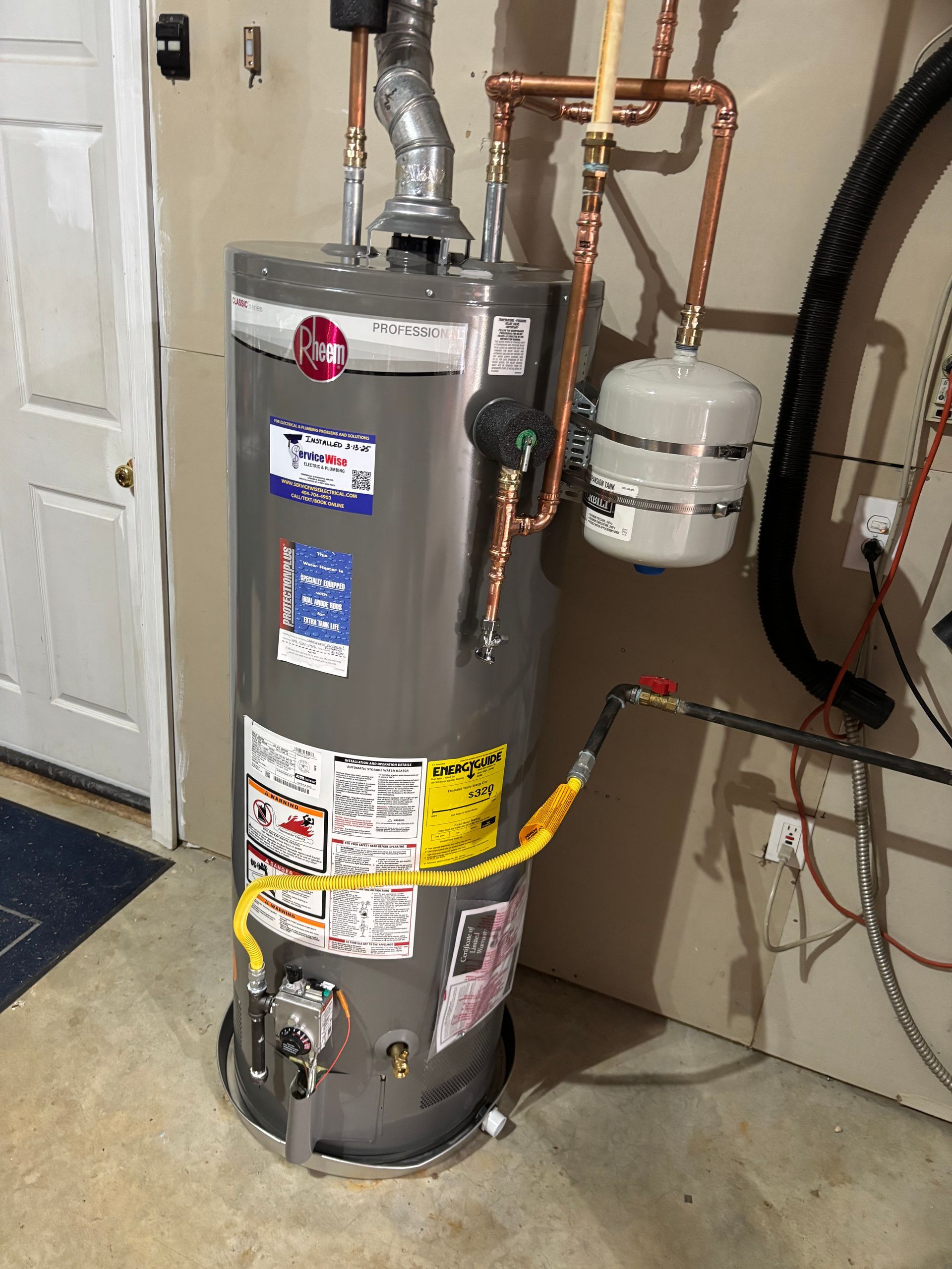 A tall, silver water heater in a garage, connected to pipes and a gas line.