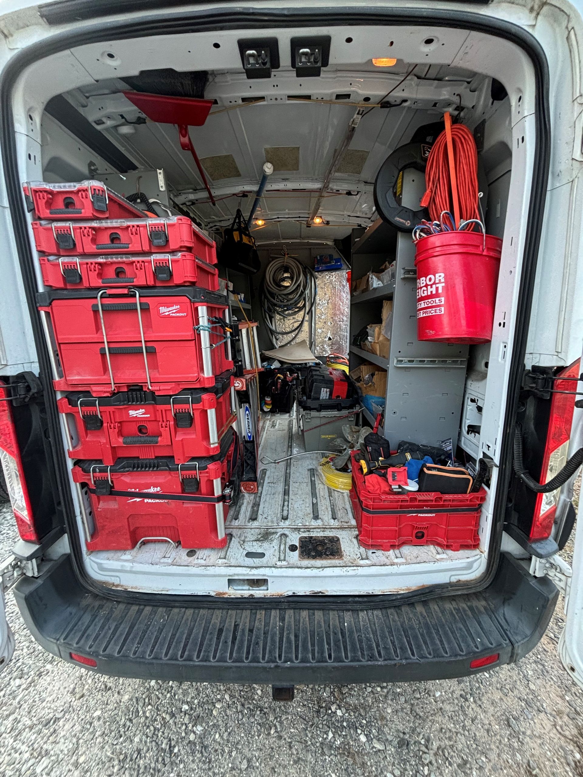 Interior of a white work van filled with red toolboxes, equipment, and shelves, ready for work.