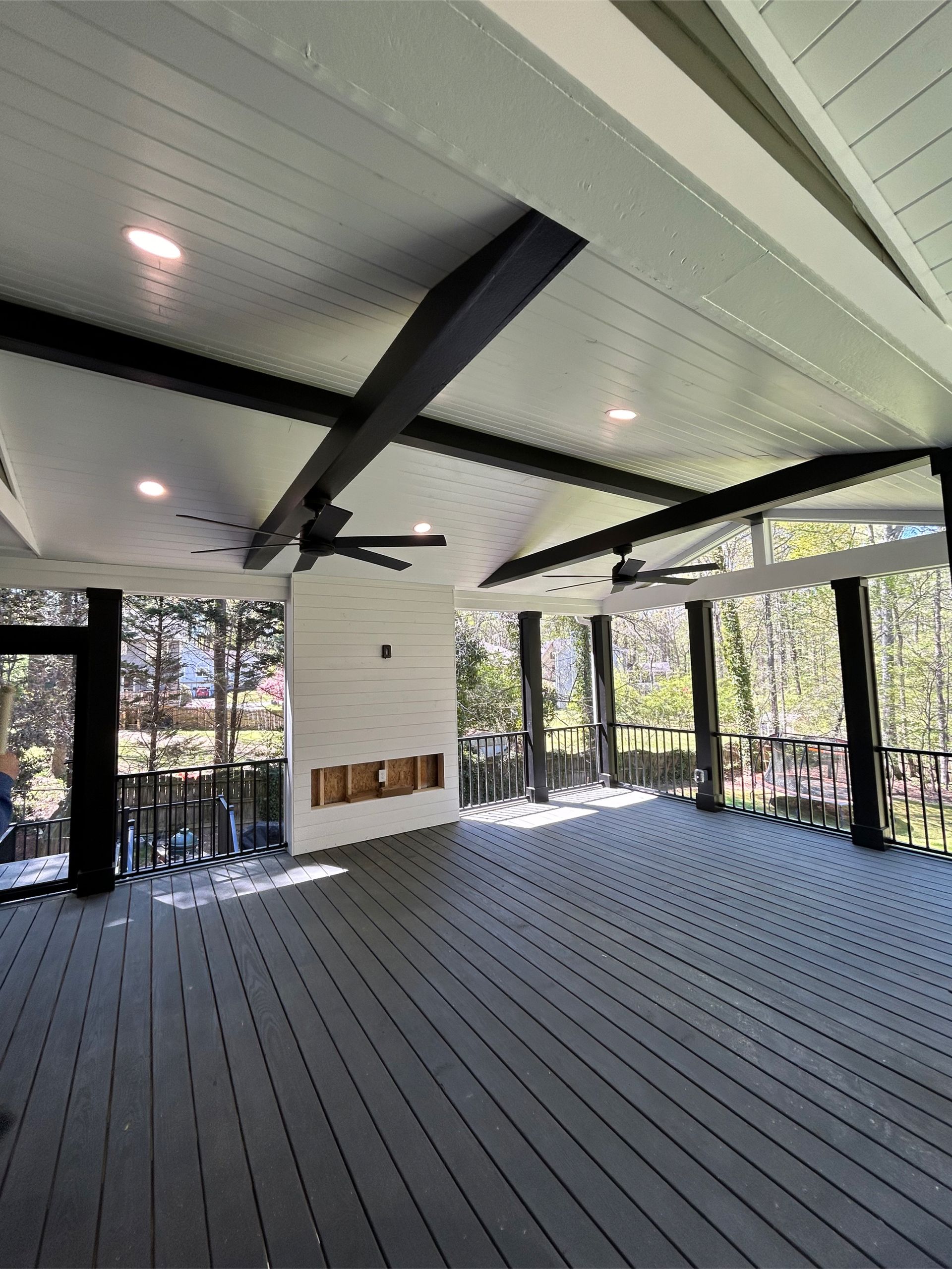 Gray deck with white ceiling, black beams and posts, and a fireplace. Outdoor setting.