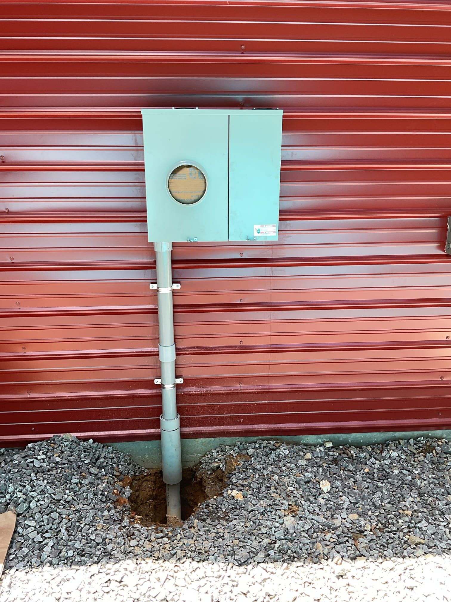 Electrical meter box on a red building, with gray conduit running down into the gravel.