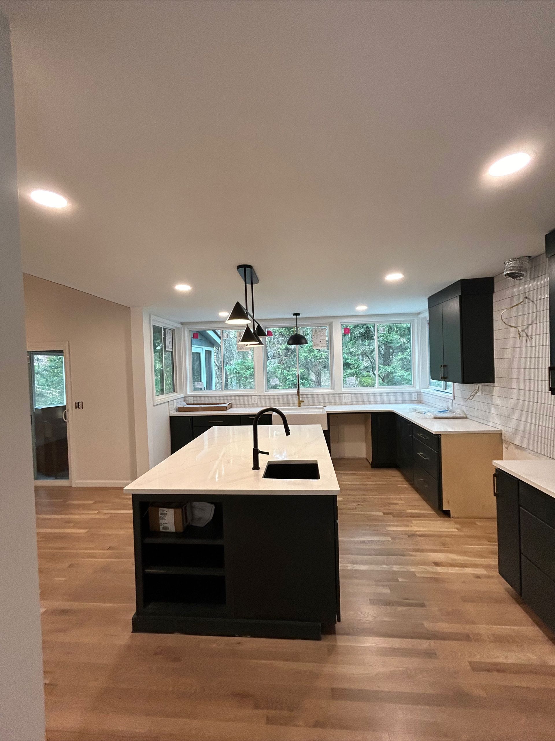 Modern kitchen with black cabinets, white countertops, and wooden floors.