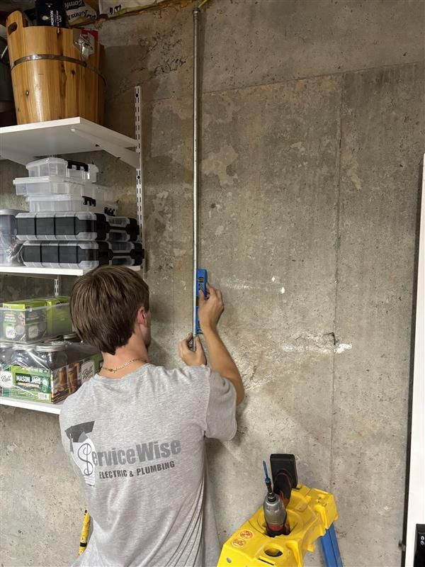 Person installing conduit on a concrete wall in a basement, using a blue tool.