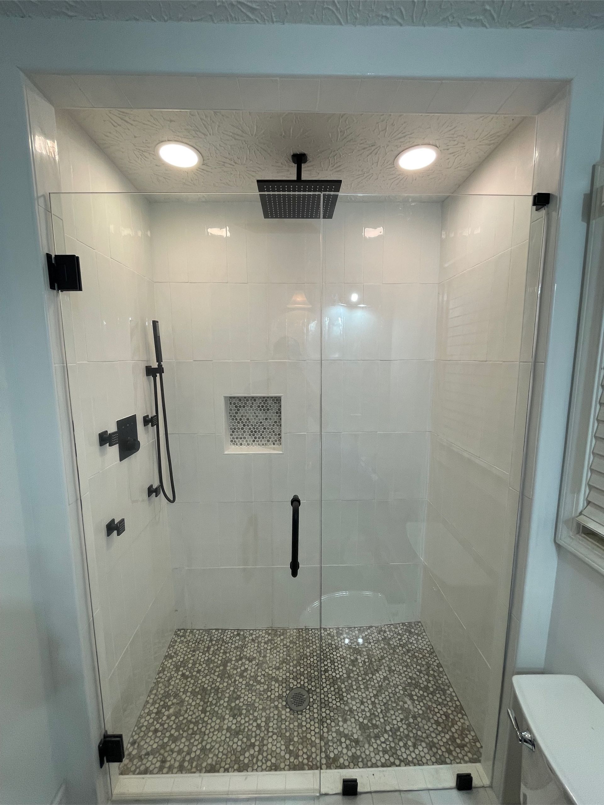 A modern glass shower with white tile walls and a pebble floor.