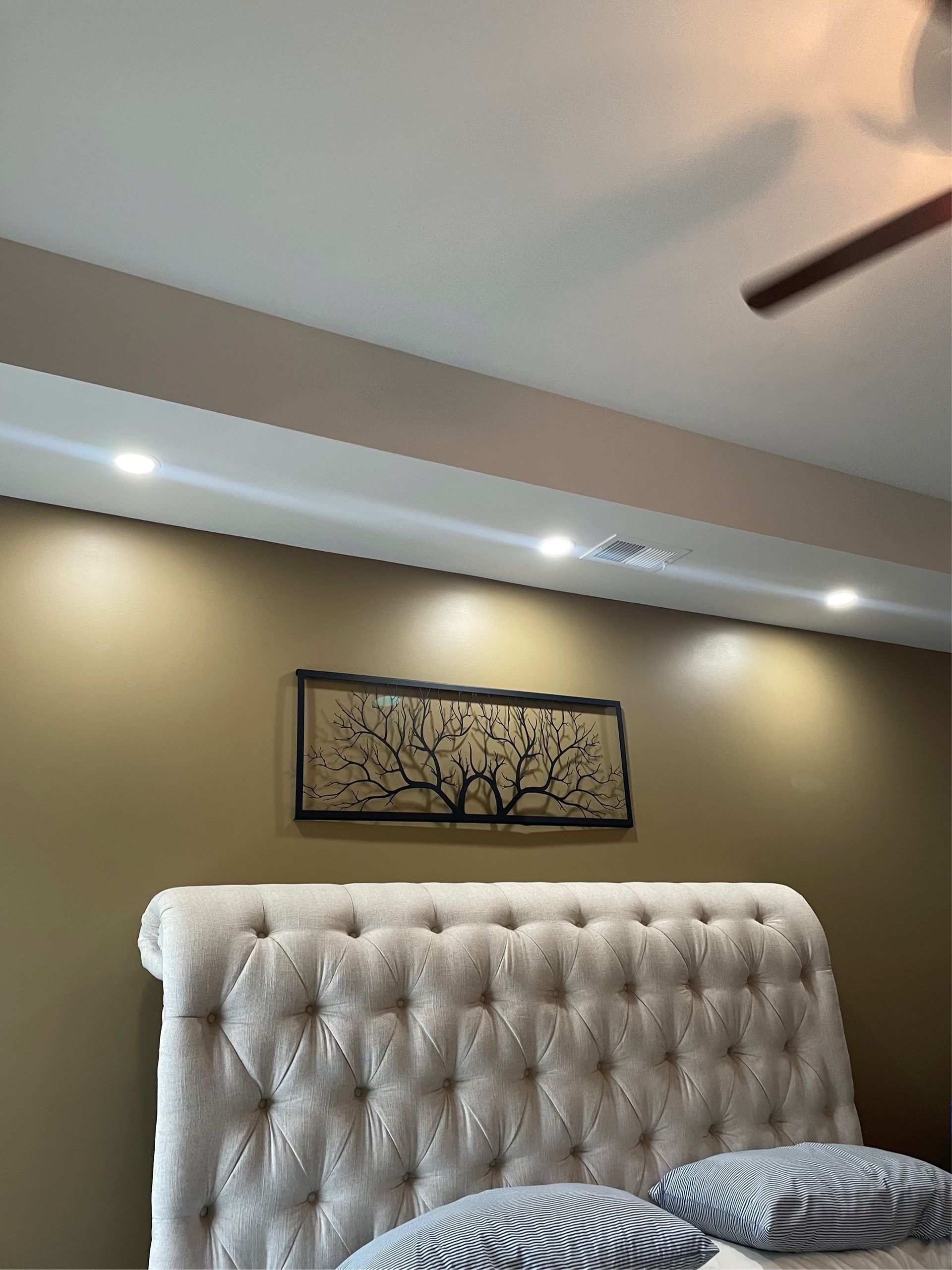 Bedroom with upholstered headboard, artwork above, and recessed lighting in the ceiling.