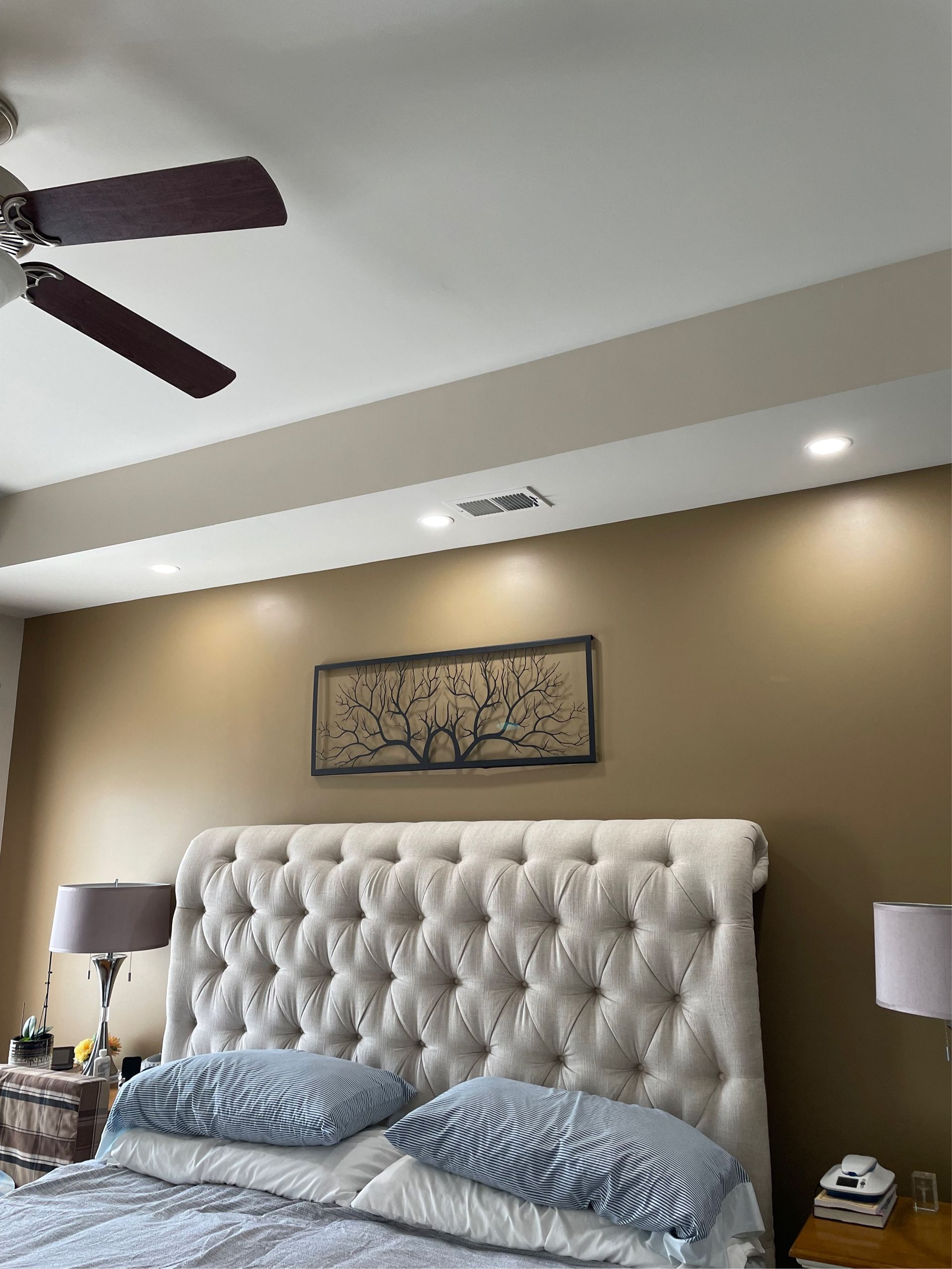 Bedroom with tufted headboard, art, recessed lighting, and ceiling fan. Light tan walls, off-white ceiling.