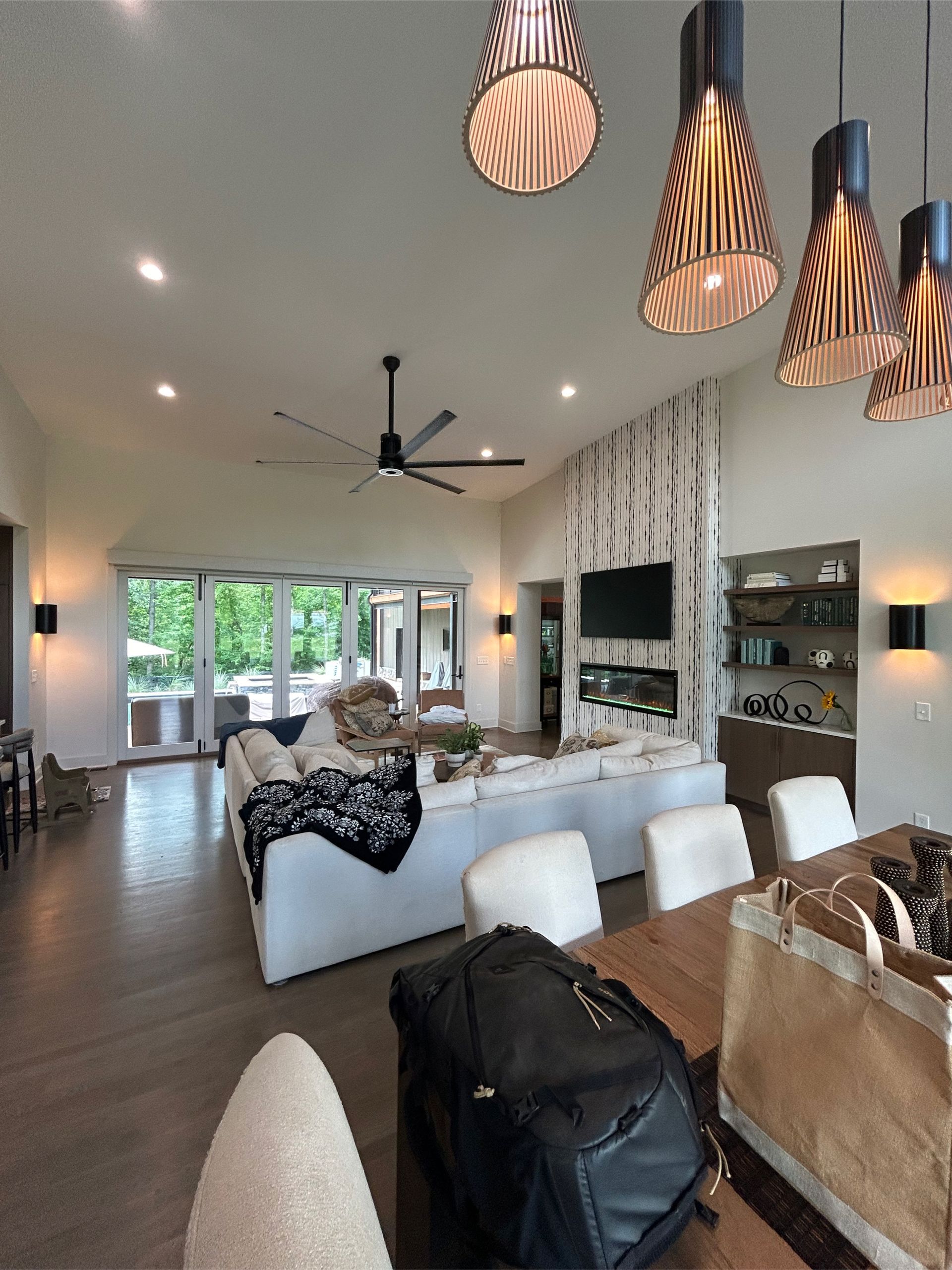 Spacious living room with white sofas, high ceilings, large windows, and decorative pendant lights.