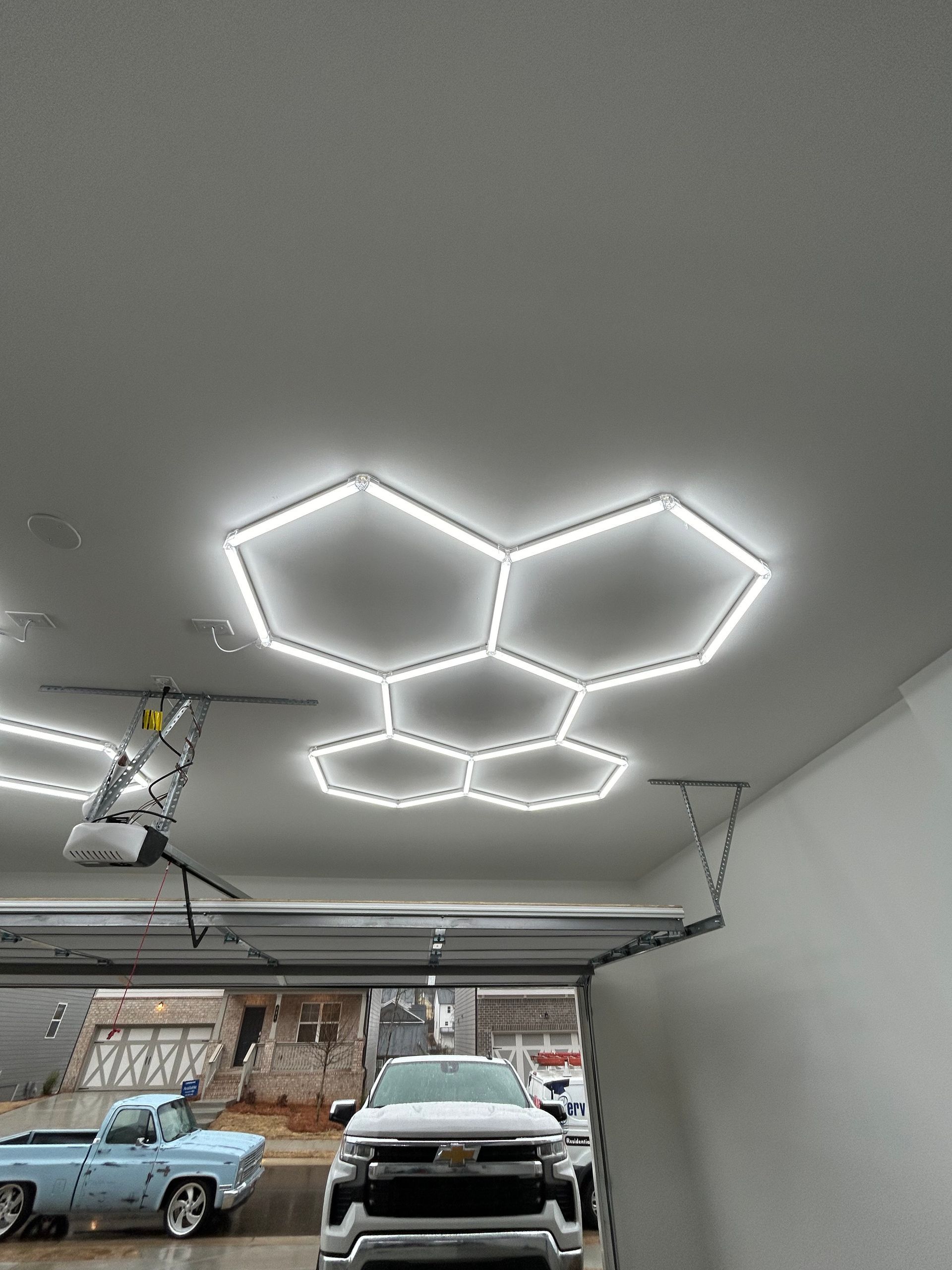 Hexagon-shaped LED lights on a garage ceiling, illuminating a car and a blue truck.