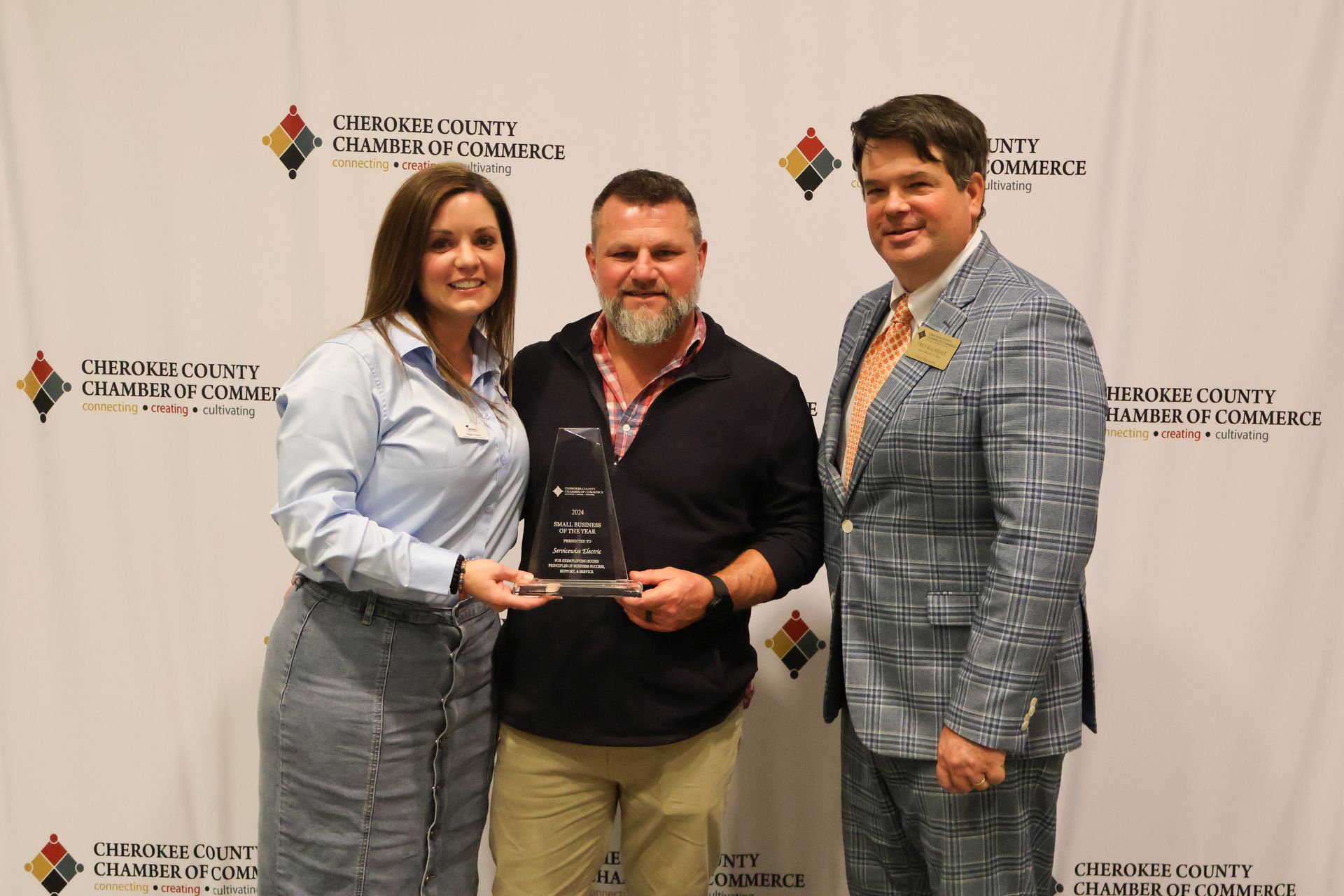Three people holding an award, posed in front of a backdrop with logos.