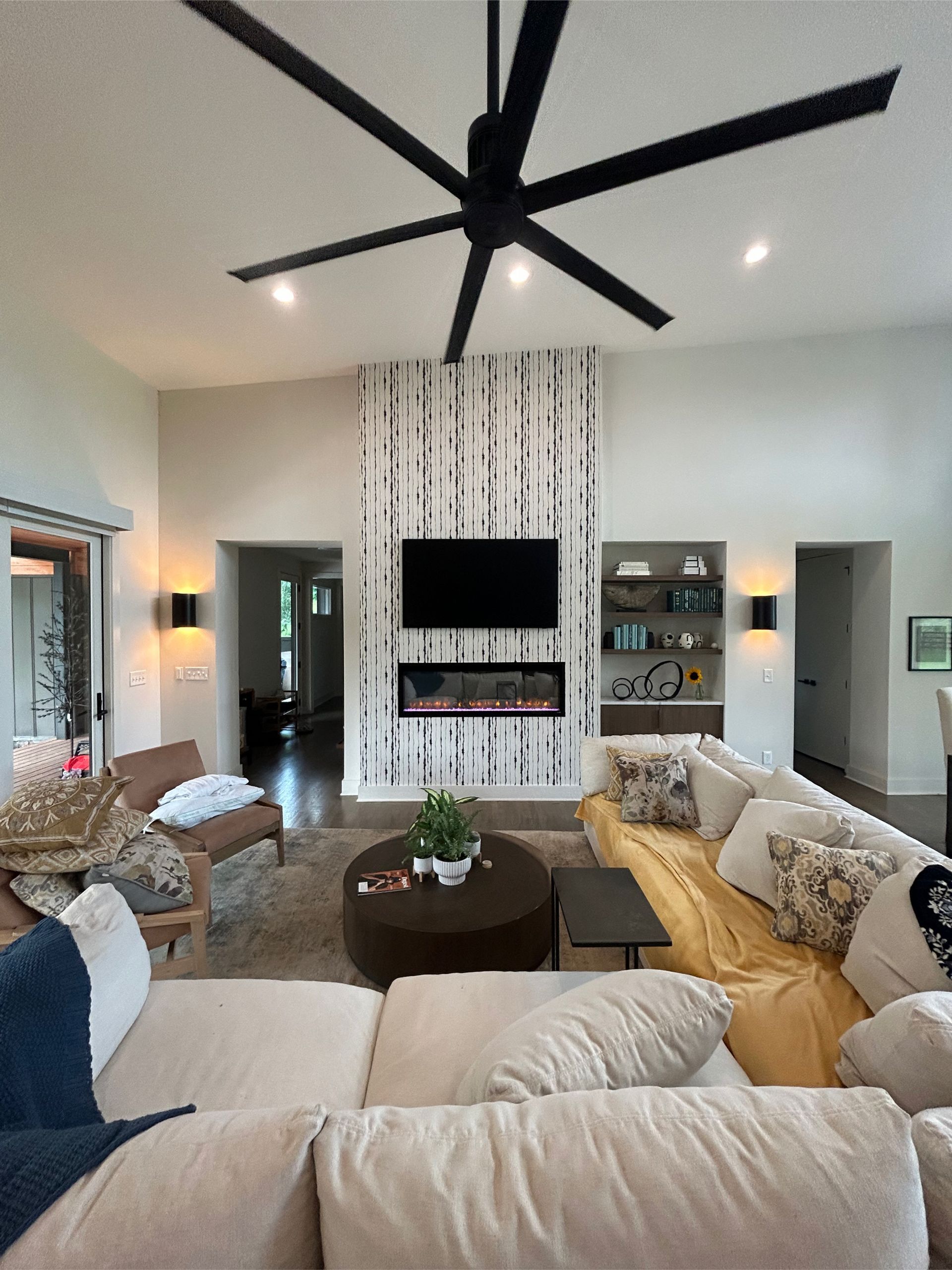 Living room with large sectional, fireplace, birch accent wall, and ceiling fan.