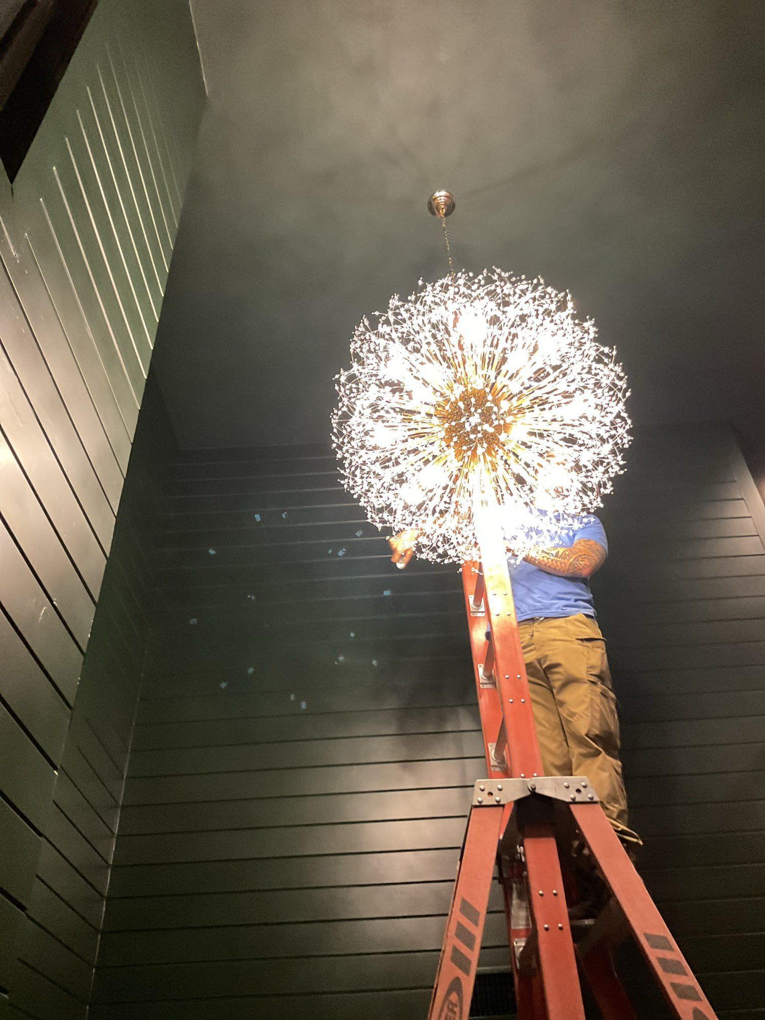 Person on a ladder installing a large, spherical light fixture on a dark wall.
