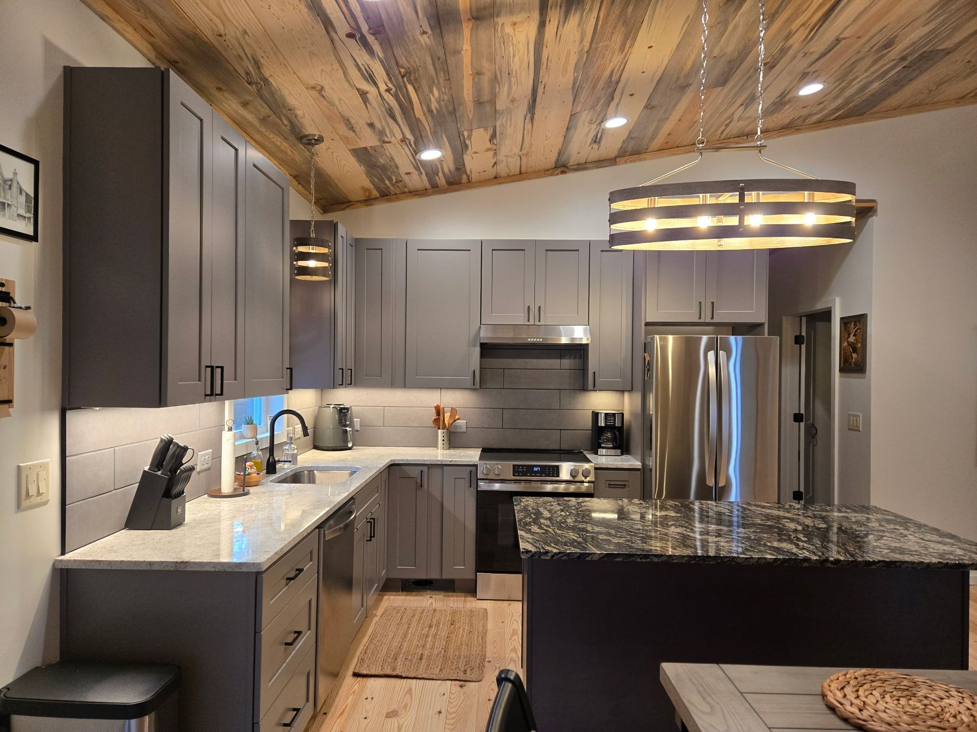 Gray kitchen with wood ceiling, stainless steel appliances, and a granite countertop island.