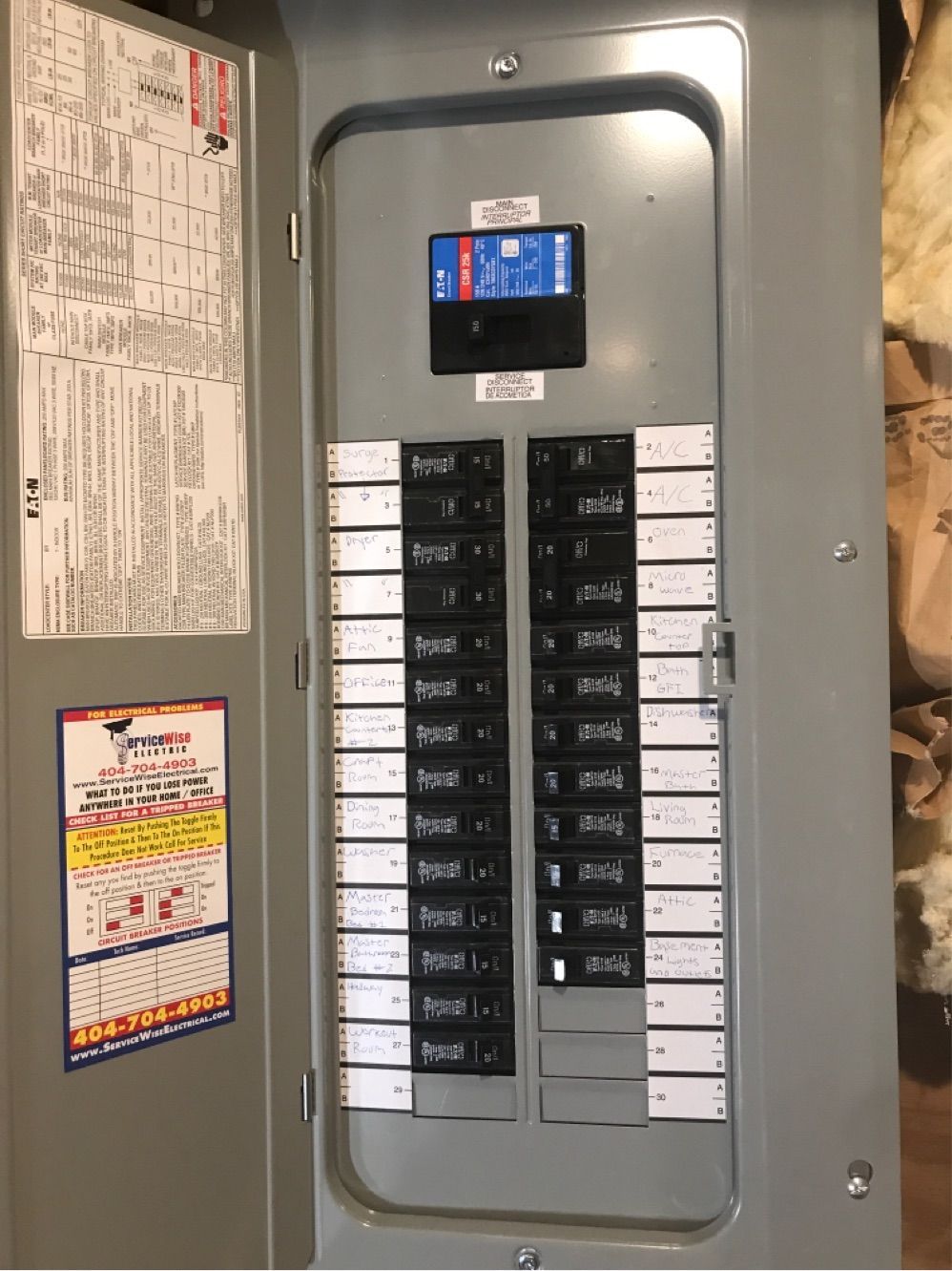 Gray electrical panel with rows of circuit breakers. A door is ajar, revealing labels.
