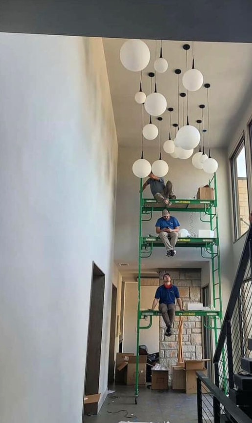 Workers on scaffolding installing globe lights in a hallway with high ceilings.