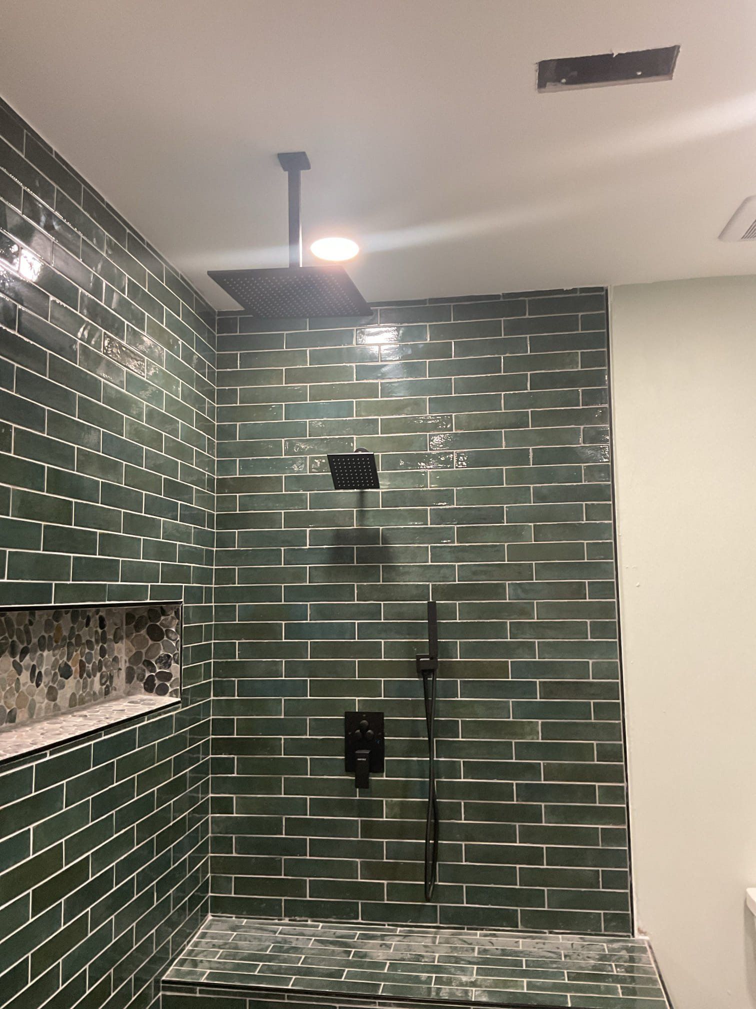 Green tiled shower with black fixtures and recessed shelving.