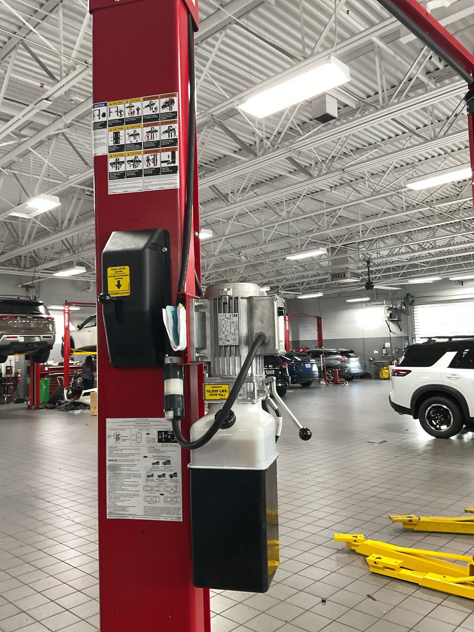 Red vehicle lift in a car repair shop; shows control panel, electrical components, and other details.