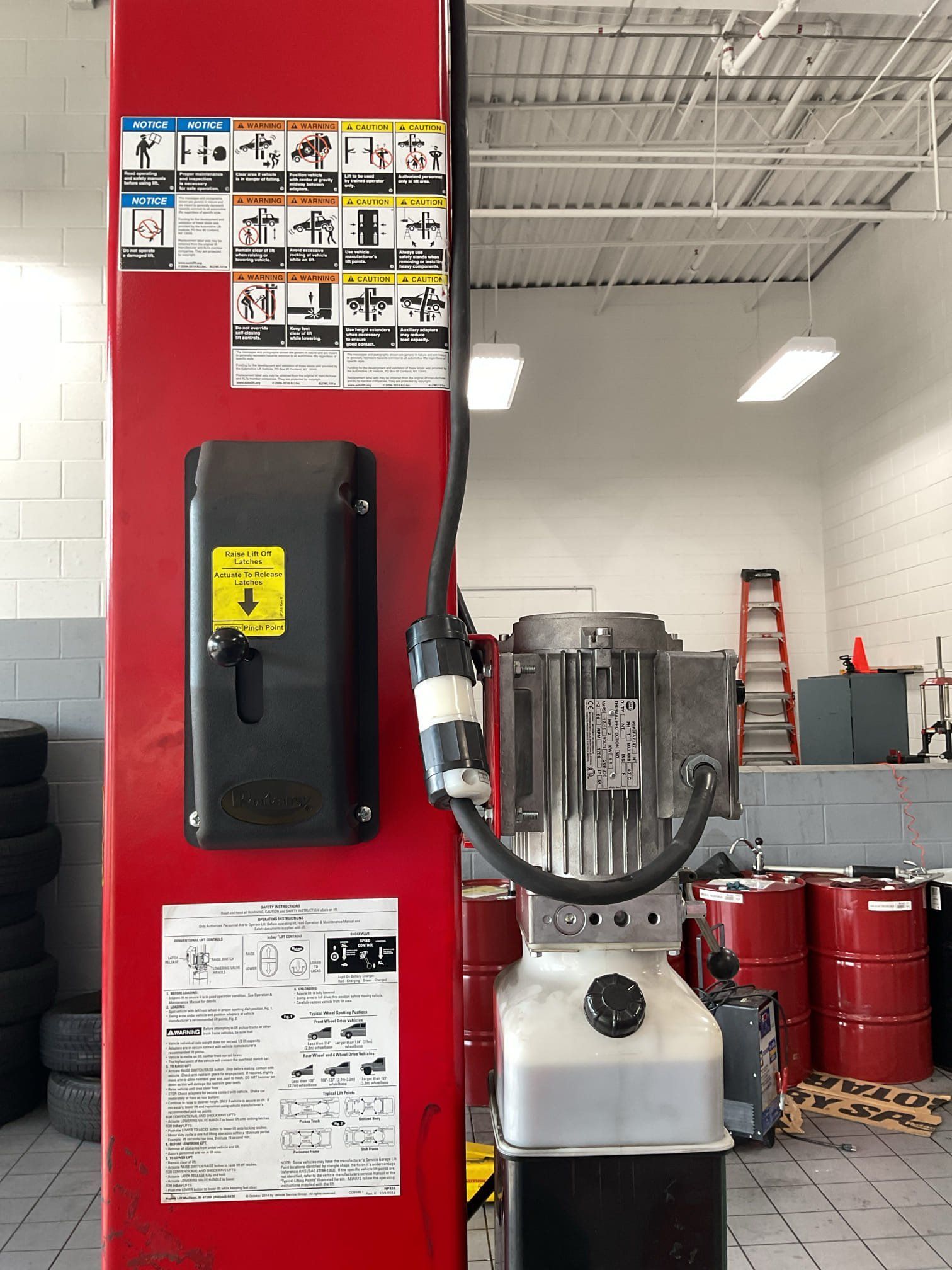 Red vehicle lift with control box, power unit, and safety instructions in a garage.