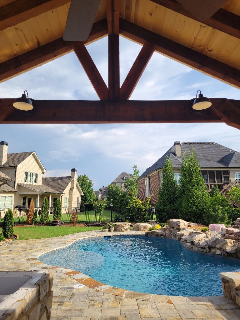 Pool under a wooden pergola with two lights. Houses and lawn in the background.