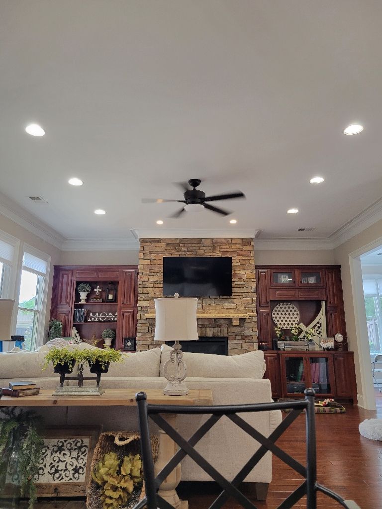 Living room with fireplace, TV, and ceiling fan; brown cabinets, white sofa, and wood floors.
