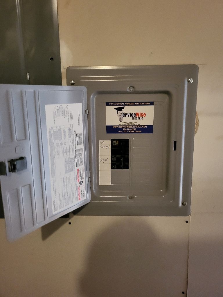 Open electrical panel with the door open, showing breakers and labels on a white wall.
