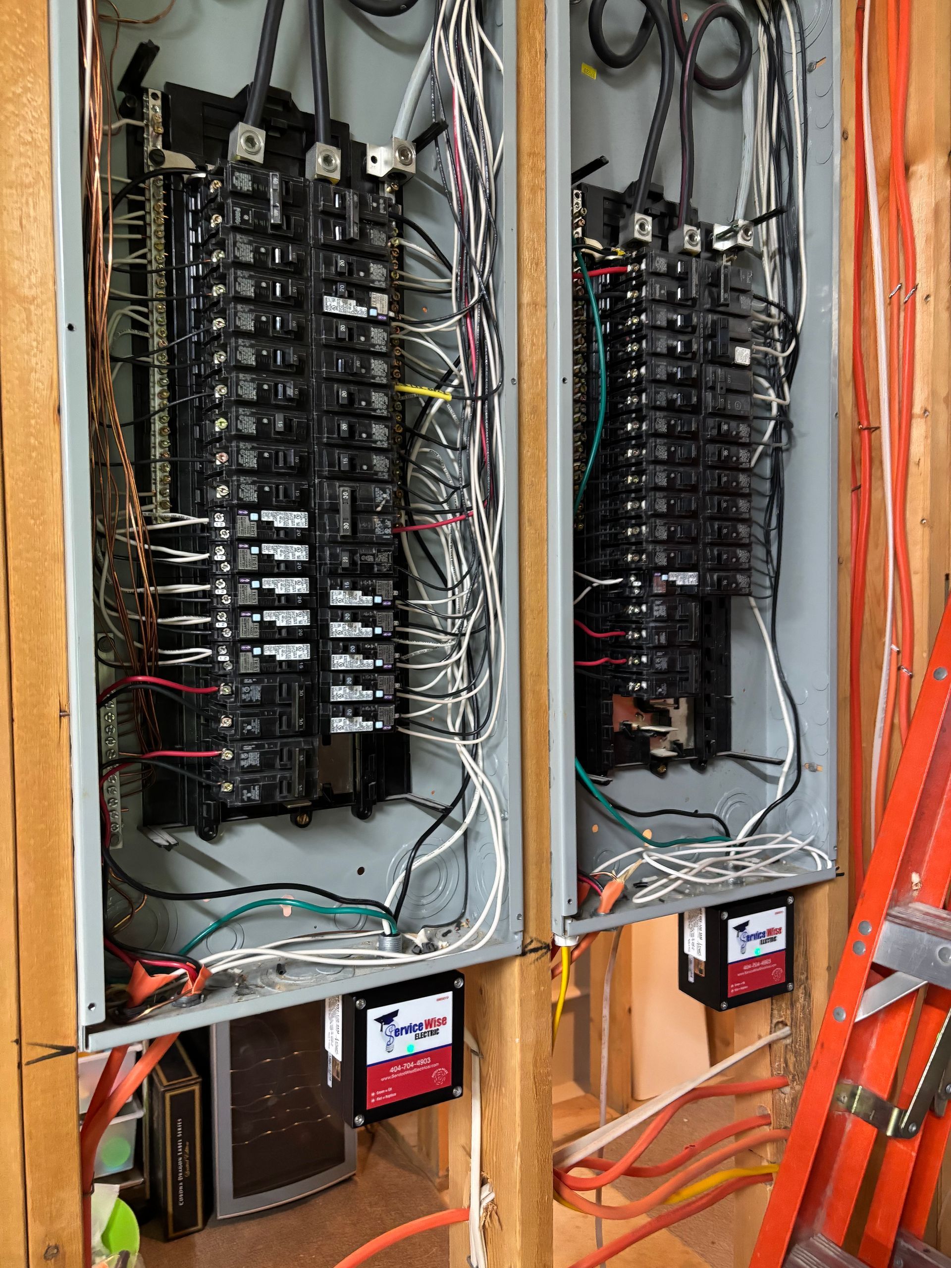 Two electrical panels with numerous wires and circuit breakers, mounted in a wooden frame.