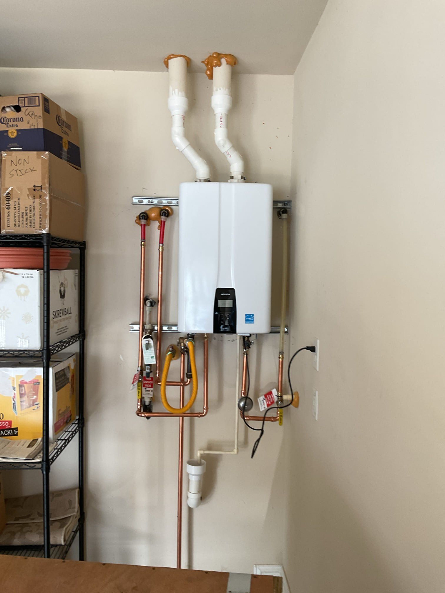 White tankless water heater mounted on a beige wall with copper pipes and venting.