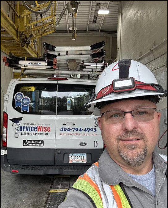 Man in a hard hat smiles, with a service van behind him.