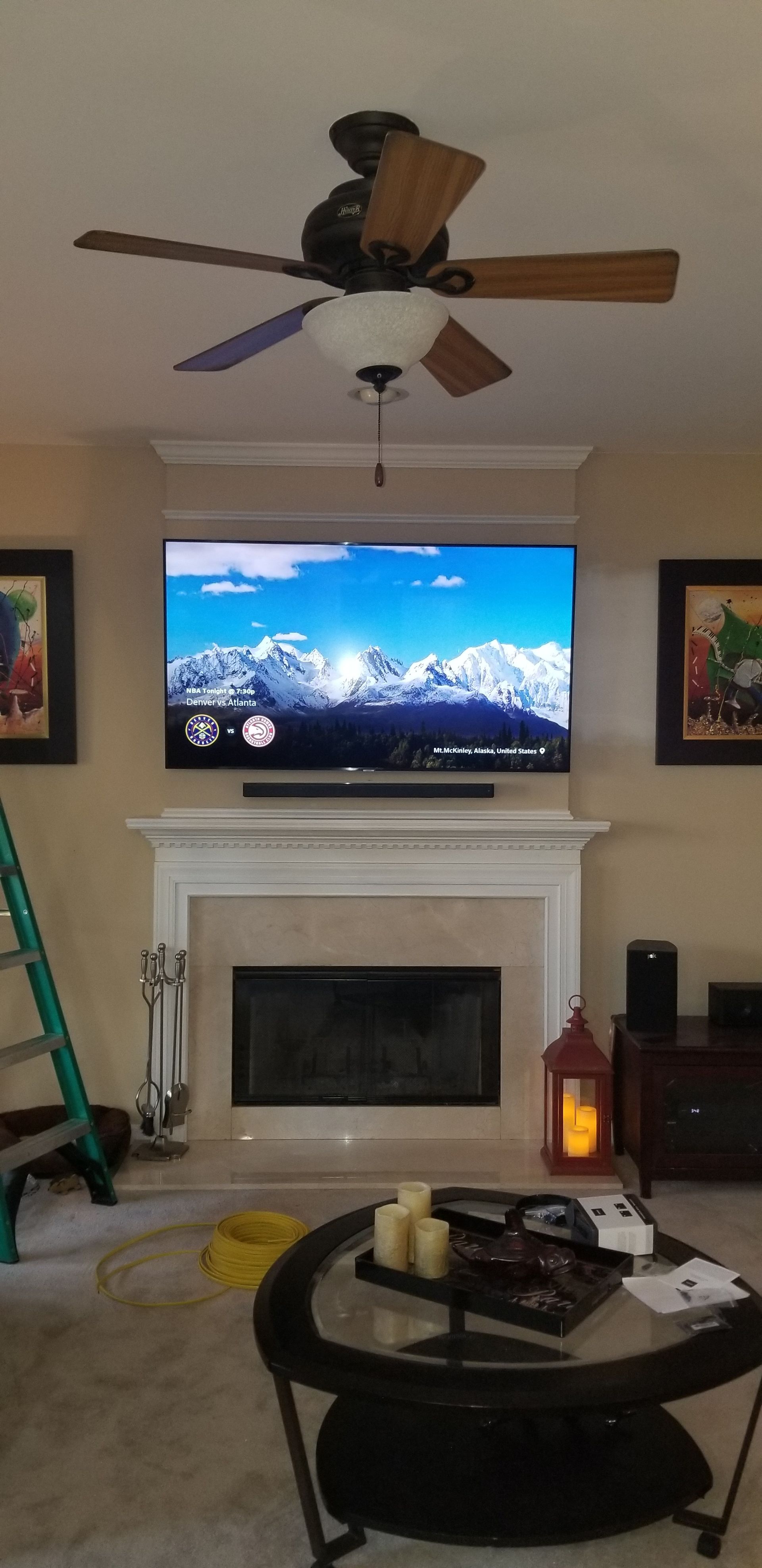 Living room with fireplace, TV, and ceiling fan. Coffee table with candles in front of the fireplace.