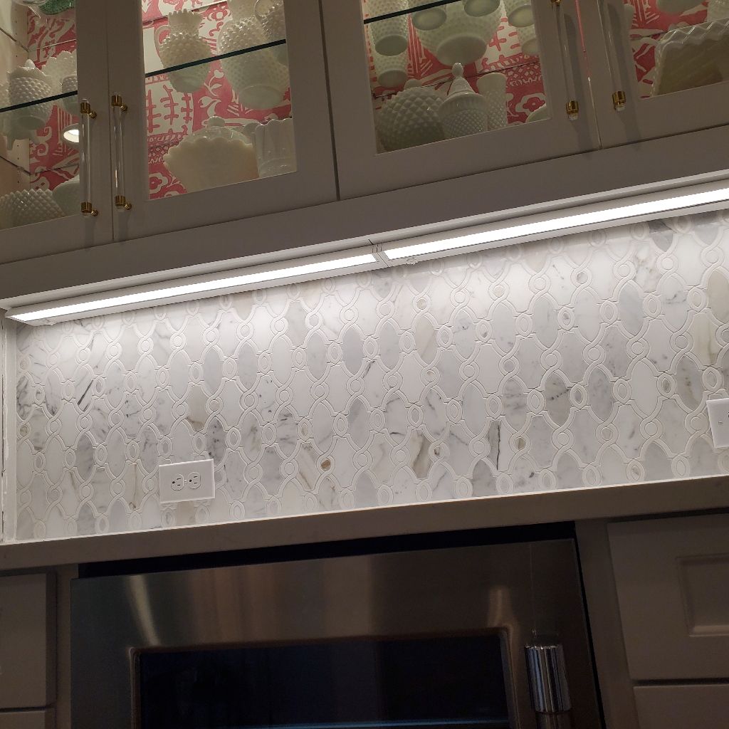 Kitchen backsplash with white mosaic tiles, under-cabinet lighting, and stainless steel oven.