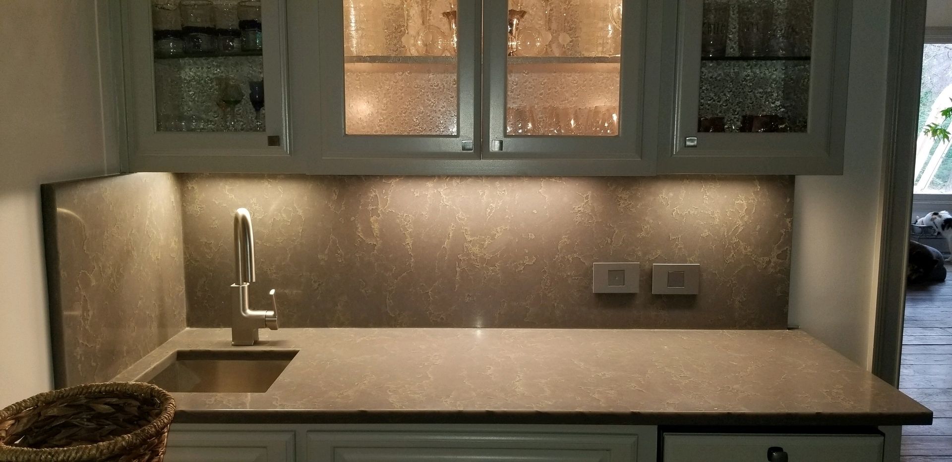 A small kitchen area with a sink, cabinetry, and a neutral-toned backsplash and countertop.