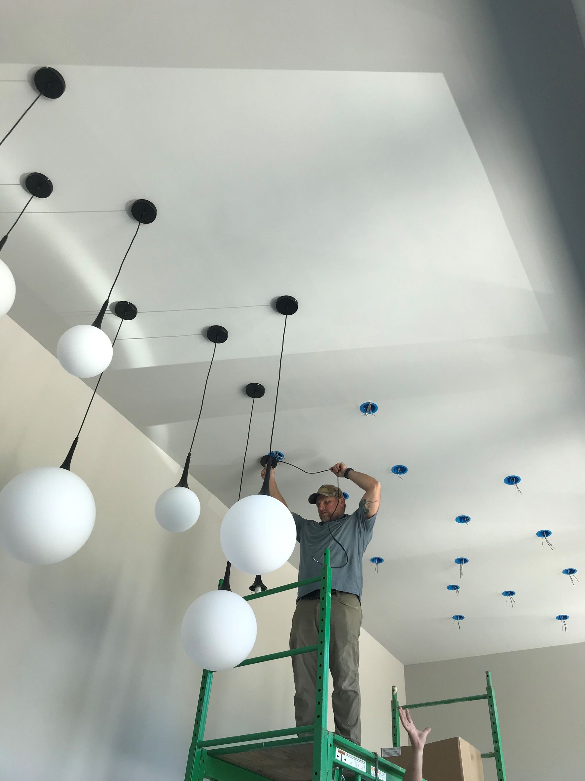 Man on scaffold installing globe lights in a room with a white ceiling and walls.